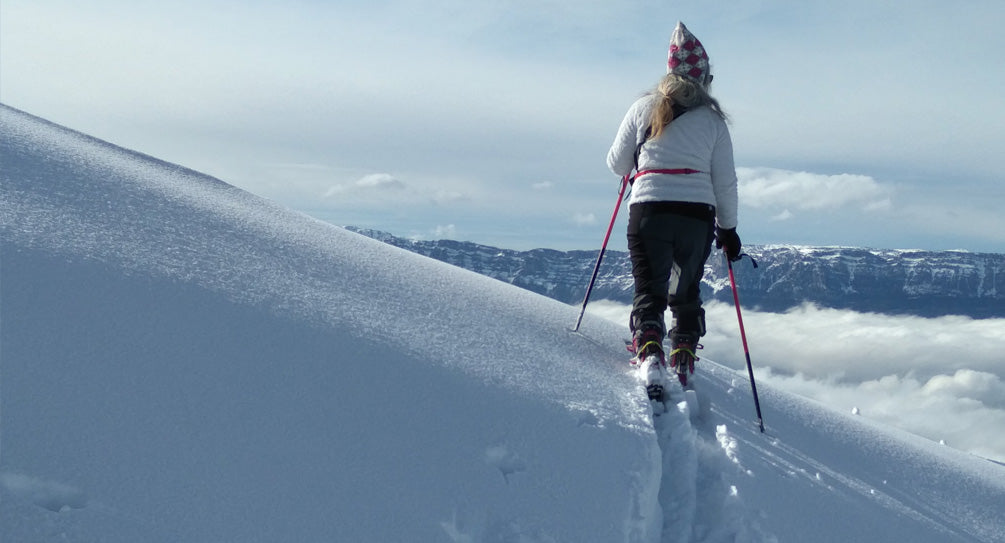 Bénédicte Allée cross-country skiing on a snowy mountain with clouds below and mountain vista in the background.