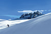 Person skiing down a snowy mountain with a clear blue sky and Dents du Midi in the background.