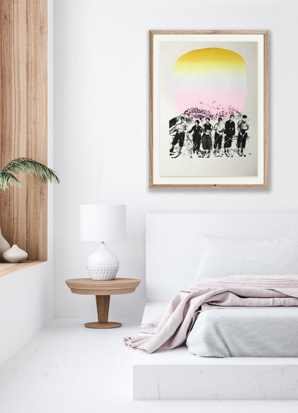 A screen print of several skiers in vintage clothing, with a stylised mountain range in the background. The colours are black, cream, pink, and yellow. Its framed on a white bedroom wall.