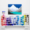 Colourful original painting of mountains above a fireplace with paint cans arranged in a pattern below it.