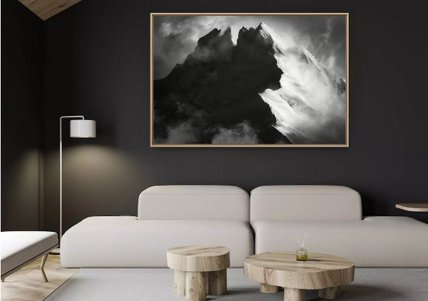 Living room with a large framed black and white painting of the Dents su Midi on the wall, a white sofa, and wooden tables.