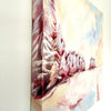 side view of oil painting. Snowscape painting depicting winter landscape hanging on wall in pastel tones of pink blue and white.
