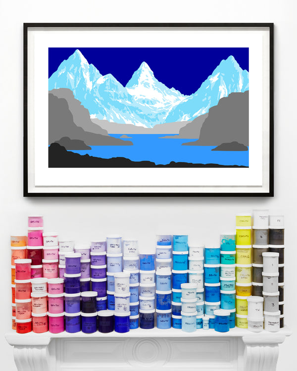 Framed wall art print of a mountain landscape with a mantel piece displaying colourful paint containers below.