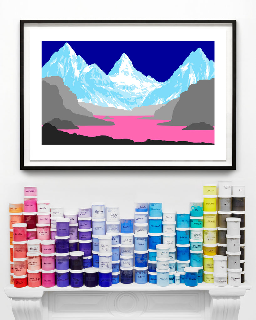 Framed landscape artwork of mountains and a lake with colourful paint cans below on a white mantel piece.