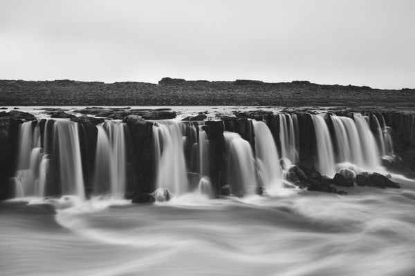 Waterfall art print. A long exposure black and white photo of the Selfoss waterfall in Iceland, featuring silky white water flowing over dark, rugged rocks.